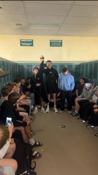 Pilafias raises the victorious Tate Frost’s hand; spectators take videos and some sit atop lockers.